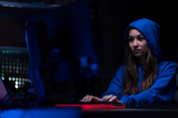 A young woman hacker by computer in the dark room at night, cyberwar concept.