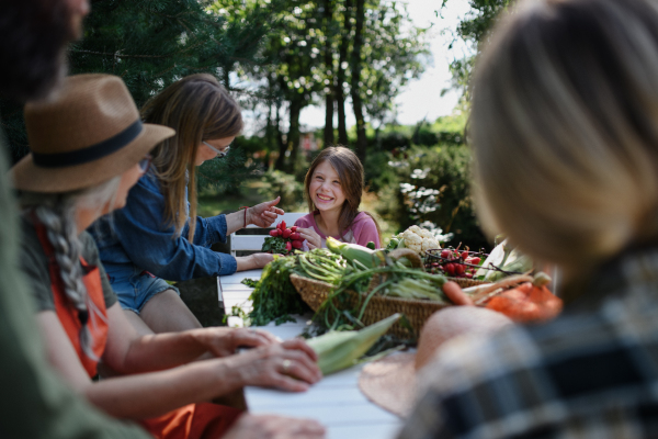 A happy farmer family sitting at table and looking at their harvest outdoors in garden.