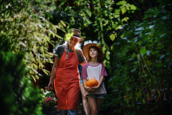 A happy little farmer girl with mother and grandmother looking at camera outdoors at garden