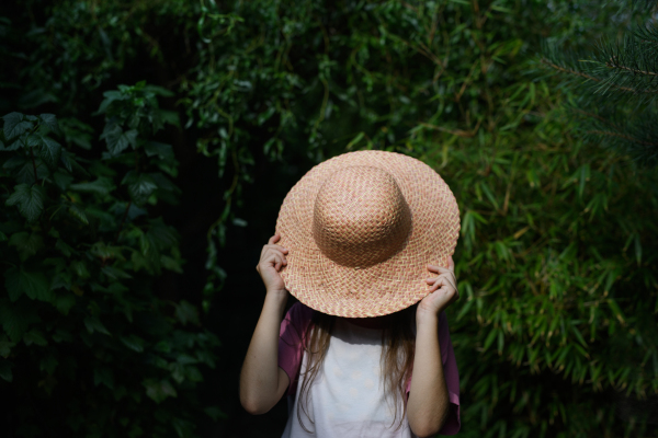 An unrecognizable little girl in hat standing outdoors at farm.