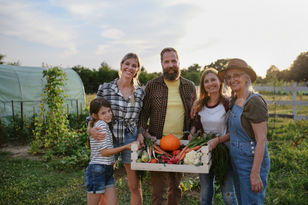 A happy farmer family looking at camera and holding their harvest outdoors in garden.