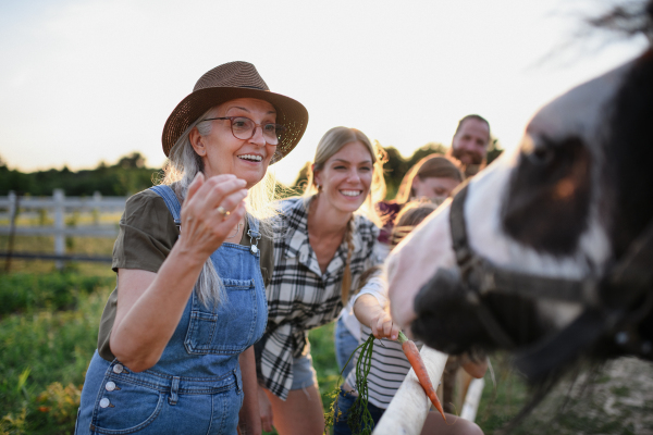 Happy farmers family feeding horse outdoors at a farm.