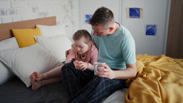 A father with his little daughter with Down syndrome sitting on bed and bonding at home.