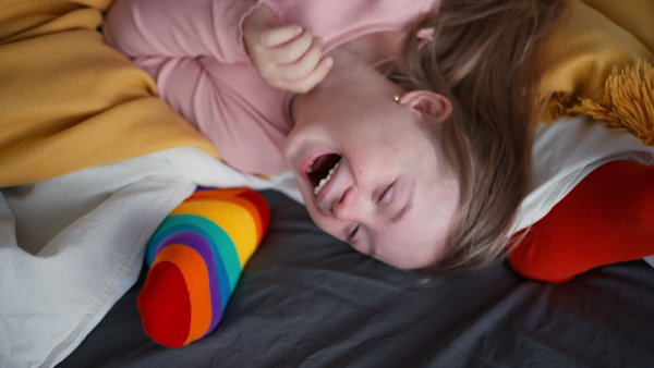 a cheerful little girl with Down syndrome lying on bed and laughing when her father is tickling her.