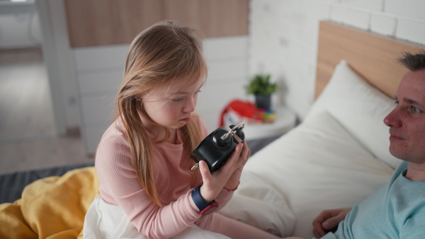 A father setting alarm clock with his little daughter with Down syndrome in bed at home.