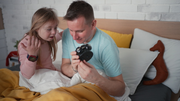 A father setting alarm clock with his little daughter with Down syndrome in bed at home.