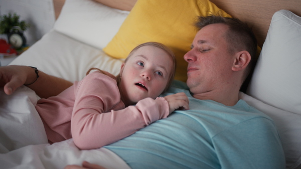 A father resting with his little daughter with Down syndrome in bed at home.