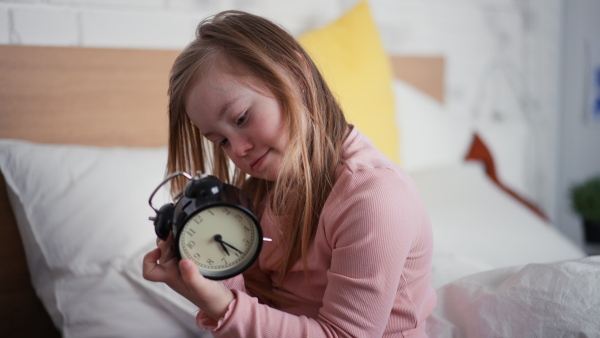 A little girl with Down syndrome playing with alarm clock at home.