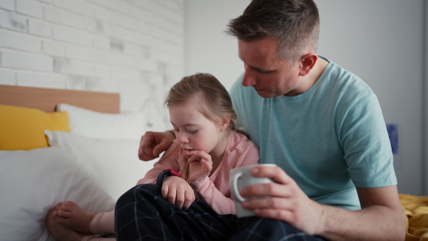 A father with his little daughter with Down syndrome sitting on bed and bonding at home.