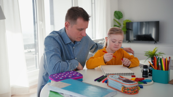 A father with his little daughter with Down syndrome drawing at home.