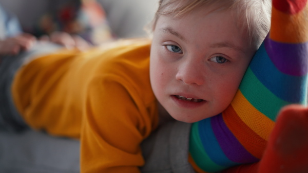 A close-up of cheerful little girl with Down syndrome lying on her father on bed and looking at camera.