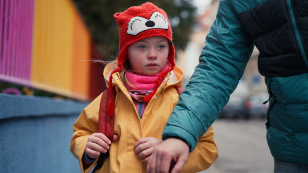 A father taking his little daughter with Down syndrome to school, outdoors in street.