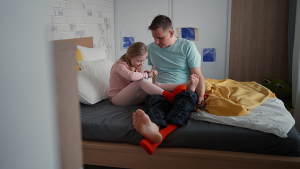 A father with his little daughter with Down syndrome sitting on bed and bonding at home.