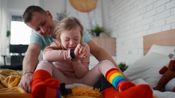 A father with his little daughter with Down syndrome sitting on bed and bonding at home.