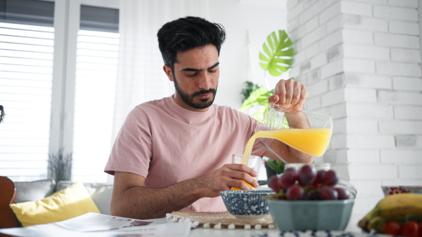 Young man pouring orange juice and reading a newspaper, morning routine concept.