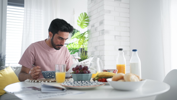 Young man having breakfast and reading a newspaper, morning routine concept.