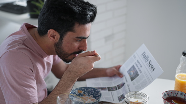 Young man having breakfast and reading a newspaper, morning routine concept.