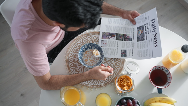 Young man having breakfast and reading a newspaper, morning routine concept.