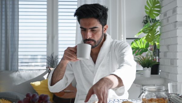 Young man in bathrobe enjoying slowly brakfast, coffee and a newspaper.