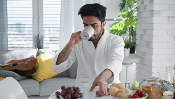 Young man in bathrobe enjoying slowly brakfast, coffee and a newspaper.