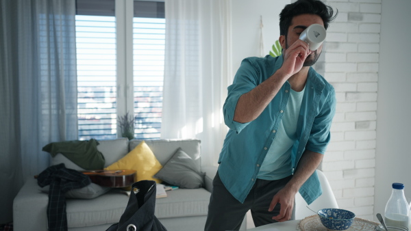 Young man hurrying up to work,finishing his breakfast, taking laptop.