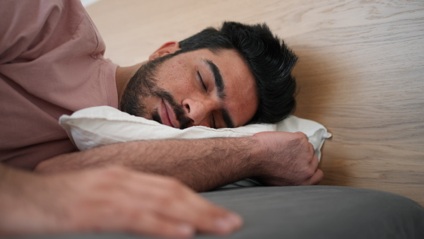 Young man waking up in his modern bedroom, turning off the alarm clock.