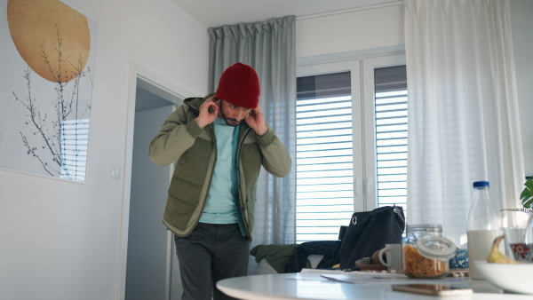 Young man hurry up to school or work, taking his bag and headphones, lefting the apartment.