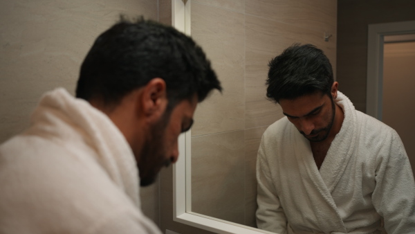 Young man in bathrobe standing in front of the mirror and brushing his teeth.