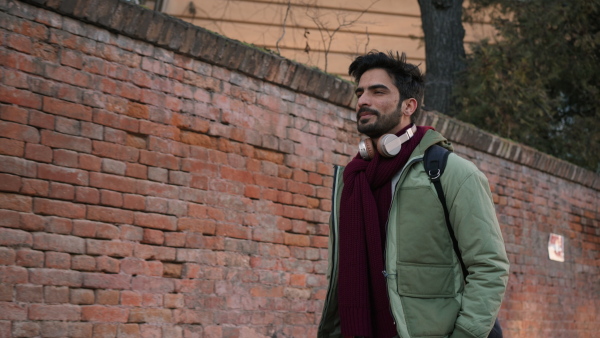 Young man with headphones walking in the street, checking time at smartphone.