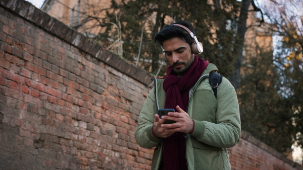 Young man with headphones walking in the street, checking his smartphone.