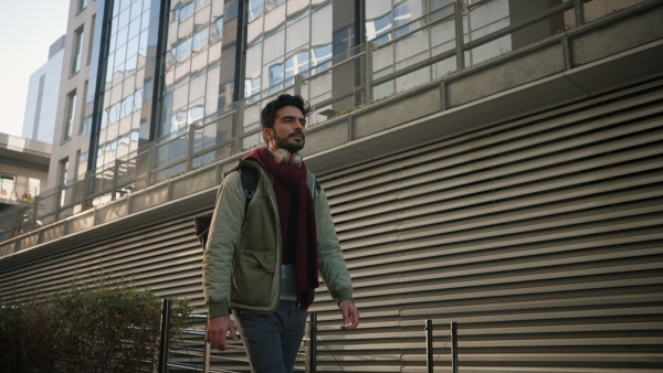 Young man with headphones and bag walking in the street, commuting concept.