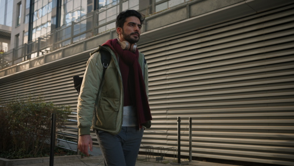 Young man with headphones and bag walking in the street, commuting concept.