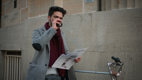 Happy young man drinking a coffee and reading newspapers near his bike, commuting cooncept.