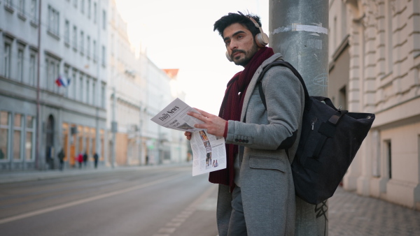 Happy young man drinking a coffee and reading newspaper on the street, commuting cooncept.