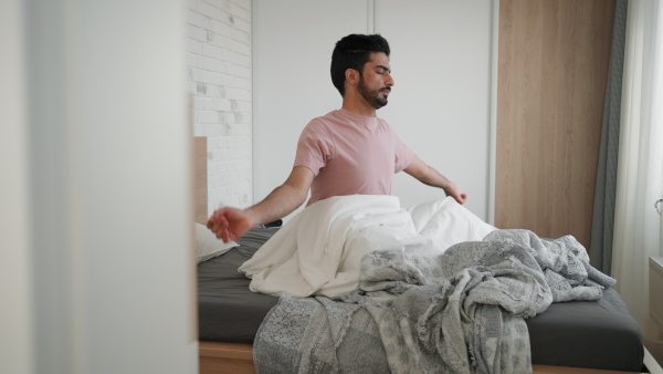 Young man waking up and stretching in a bed.