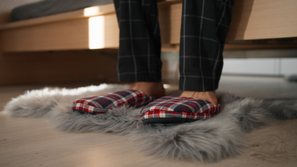 Close up of man putting on slippers and standing up from a bed.