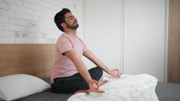 Young man doing yoga and meditation at his bed.