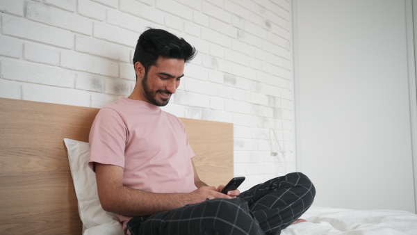 Happy young man in love sitting on bed and chatting.