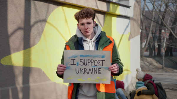 A protest against Russian invasion of Ukraine. Man holding anti war banner near refugee camp.