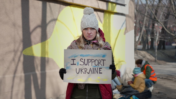 A protest against Russian invasion of Ukraine. Woman holding anti war banner near refugee camp.