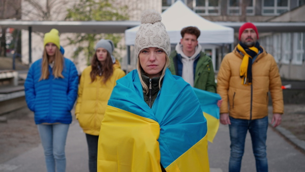 A protest against Russian invasion of Ukraine. People wrapped in Ukrainian flag in street.