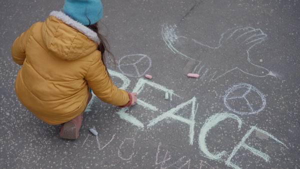 A top view of little girl writing peace with chalk. Protest against Russian invasion of Ukraine.