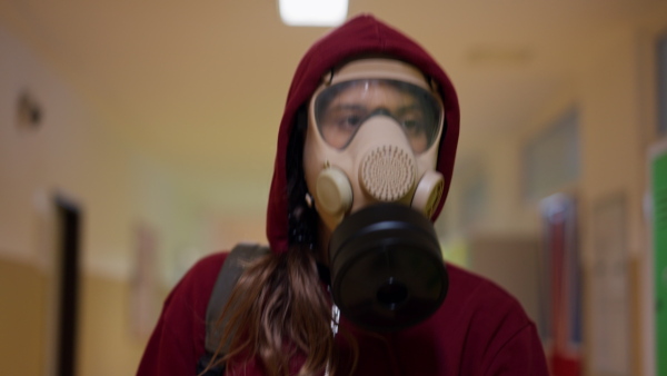 A young student in gas mask looking at camera at school.