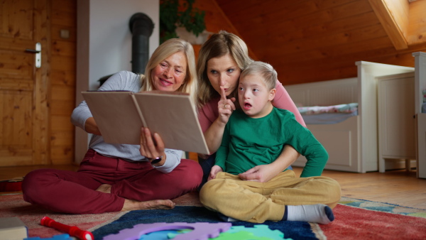 A boy with Down syndrome with his mother and grandmother looking at family photo album at home.