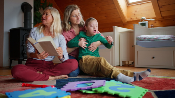 A boy with Down syndrome with his mother and grandmother trying to read book together at home.