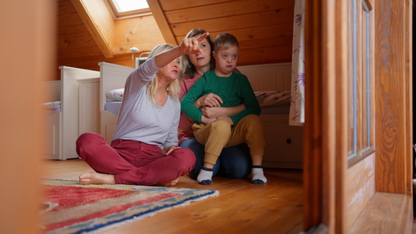 A child with Down syndrome with his mother and grandmother looking at family photo album at home.