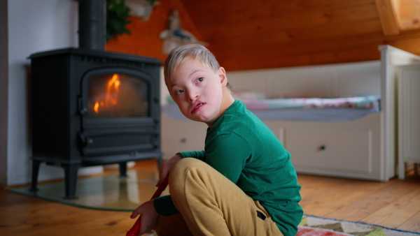 A little boy with Down syndrome sitting in front of fireplace at home.