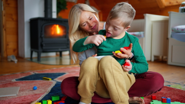 A happy boy with Down syndrome sitting on floor and hugging with his grandmother at home