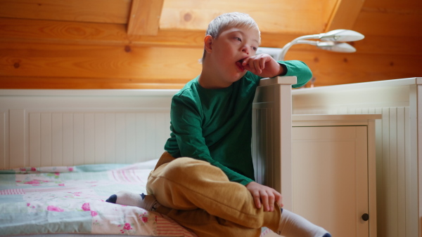 A little boy with Down syndrome sitting in front of fireplace at home.