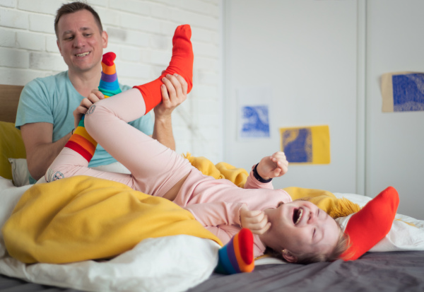 a cheerful little girl with Down syndrome lying on bed and laughing when her father is tickling her.